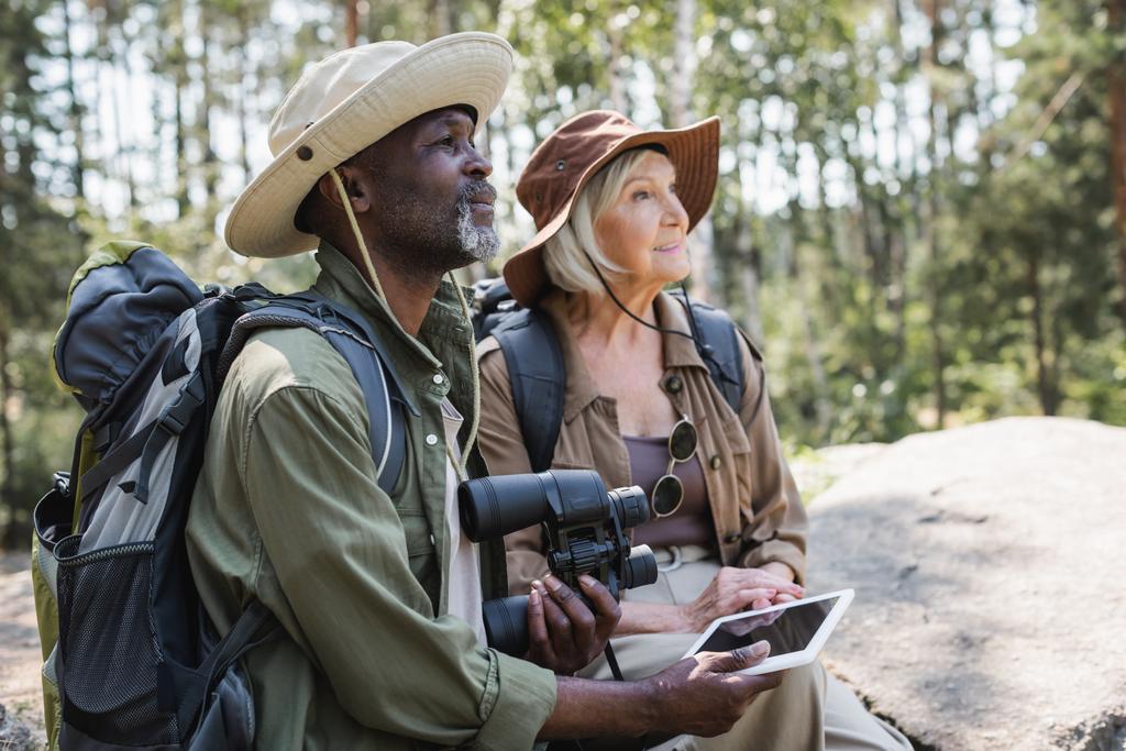 Afrikalı Amerikalı turist elinde dijital tablet ve karısının yanında dürbün tutuyordu.  - Fotoğraf, Görsel