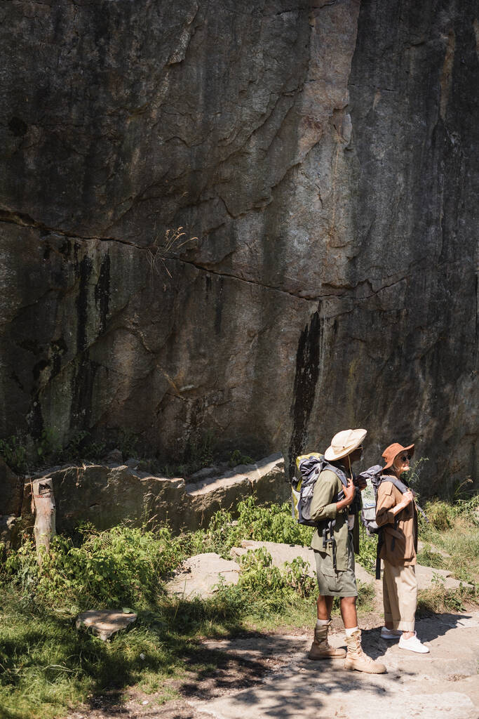 Interracial tourists with backpacks standing near cliff  - Photo, Image