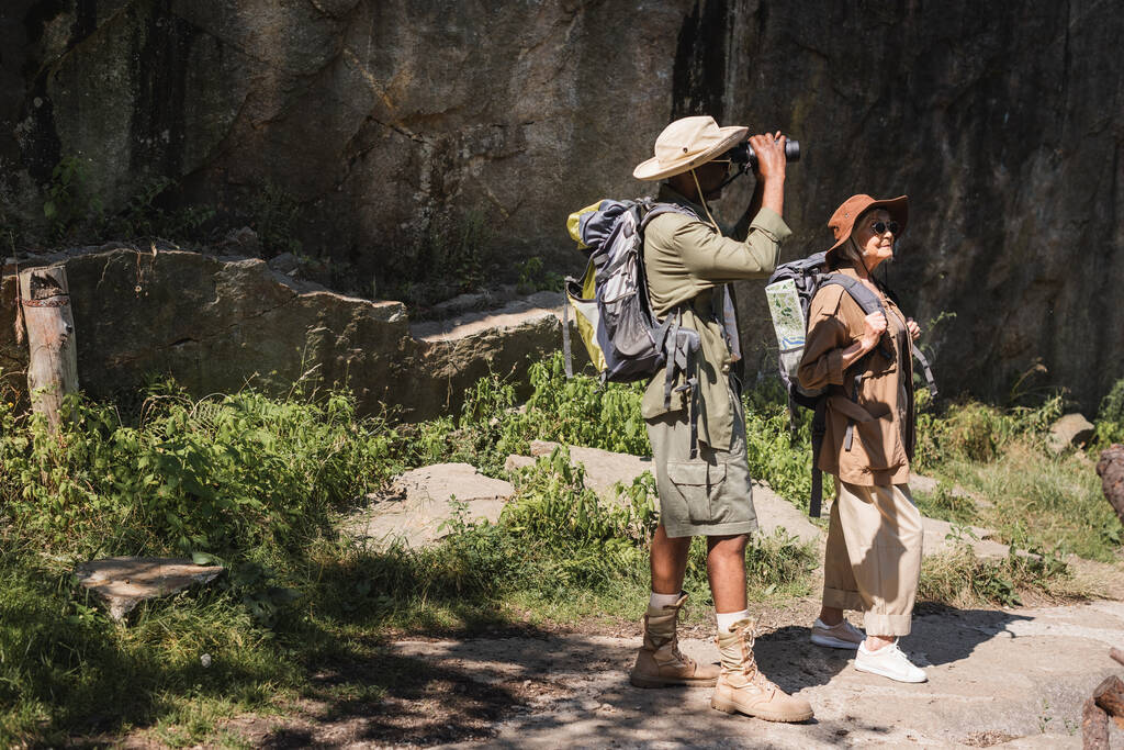 Afrikai amerikai férfi látszó bár távcső közelében feleség hátizsák és szikla - Fotó, kép