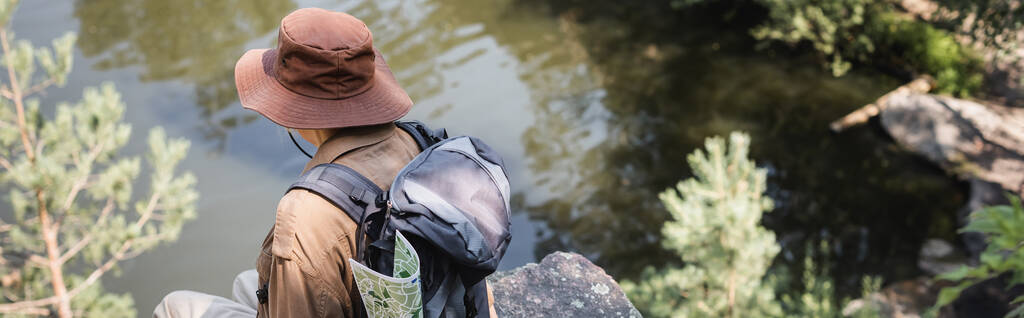 Старший турист в капелюсі з рюкзаком, що сидить на скелі біля озера, банер
  - Фото, зображення