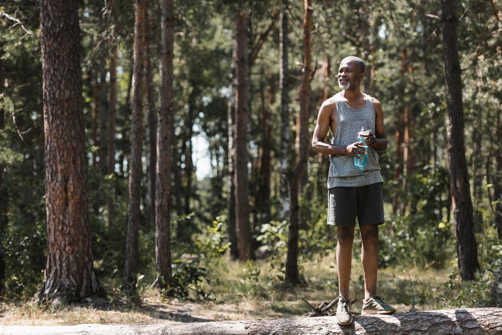 Positive afrian american sportsman holding sports bottle in forest  - Photo, Image