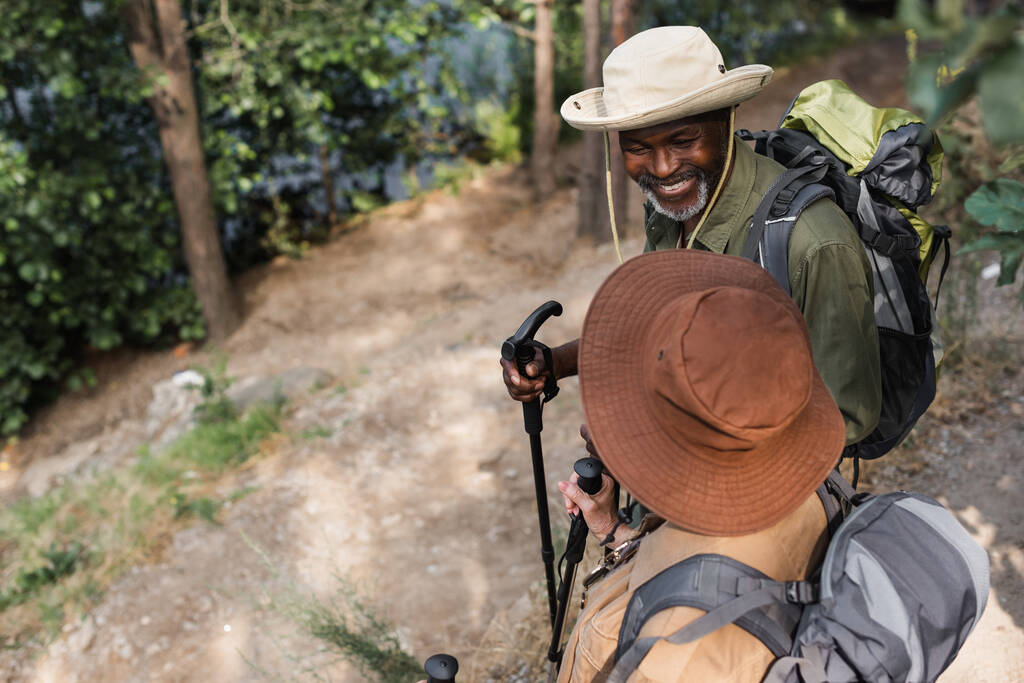 Pozitif Afrika kökenli Amerikalı turist, yürüyüş direkleri ile ormanda sırt çantasıyla karısına bakıyor.  - Fotoğraf, Görsel