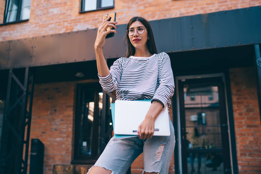 Millenniumi nő szemüveg kattintva szelfi képek segítségével elülső kamera okostelefon eszköz, női blogger, hogy online video konferencia csevegni követőivel a digitális nomád életmód - Fotó, kép