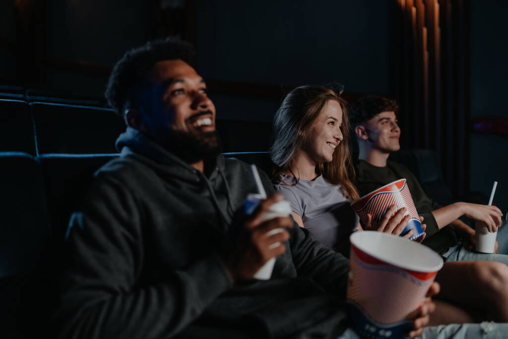 Wesoła młoda para z popcornem w kinie, rozmawiająca. - Zdjęcie, obraz