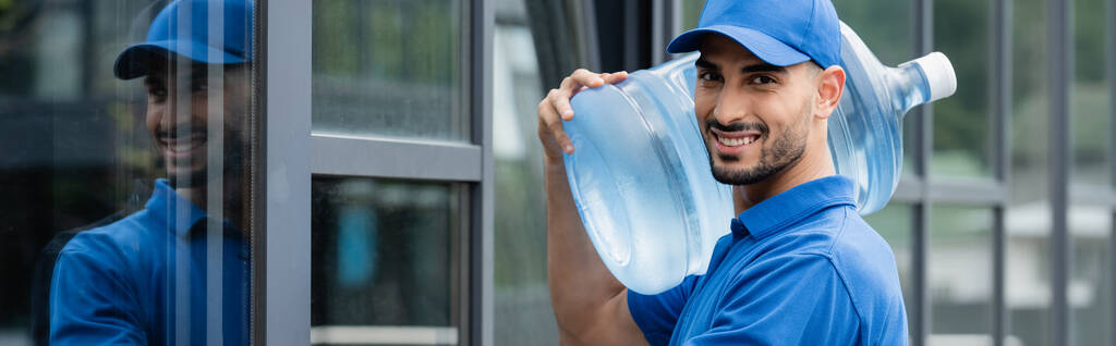 Courrier arabe souriant tenant bouteille avec de l'eau près du bâtiment, bannière  - Photo, image