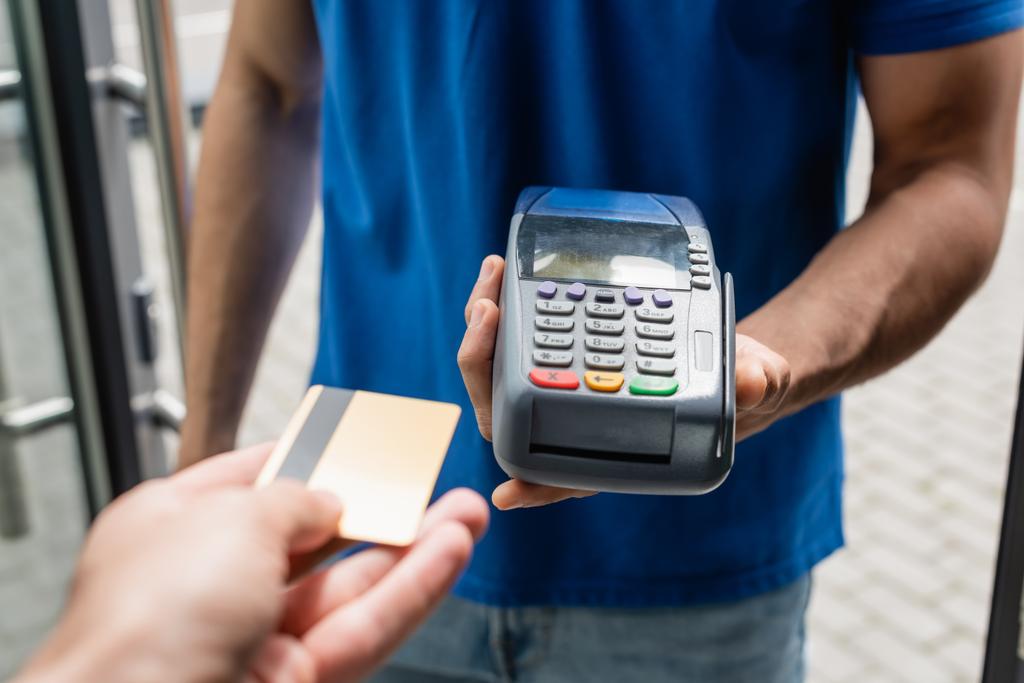 Обрезанный вид человека, держащего кредитную карту возле курьера с платежным терминалом  - Фото, изображение