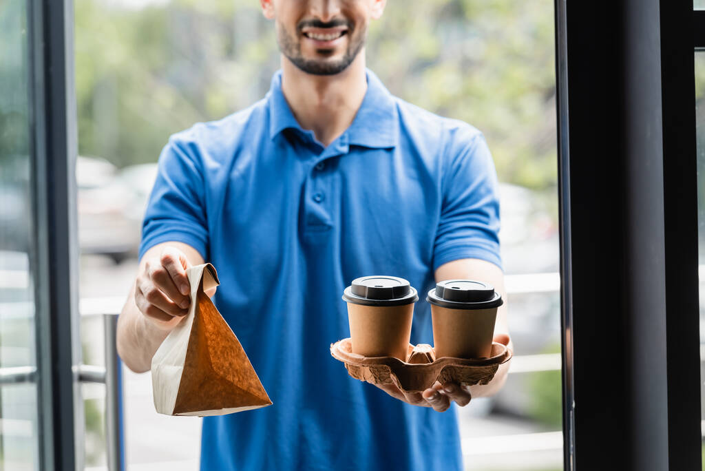 Περικοπή άποψη του καφέ για να πάει και χάρτινη σακούλα στα χέρια του θολή courier  - Φωτογραφία, εικόνα