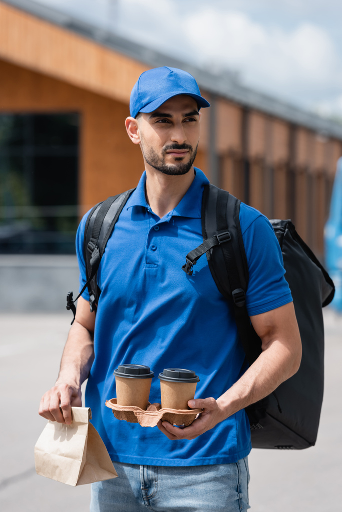 Молодий арабський есмінець тримає каву, щоб піти і паперовий мішок на відкритому повітрі
  - Фото, зображення
