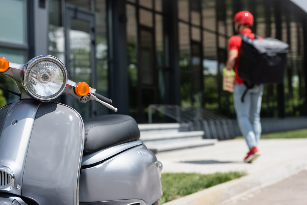 Scooter cerca de mensajero borroso con mochila al aire libre  - Foto, Imagen