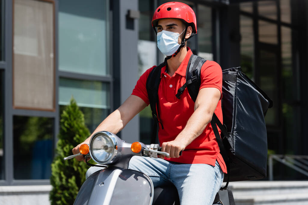 Correio muçulmano em máscara médica com mochila térmica montando scooter ao ar livre  - Foto, Imagem