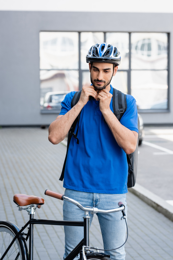 Mensajero musulmán con mochila con casco cerca de la bicicleta al aire libre  - Foto, imagen