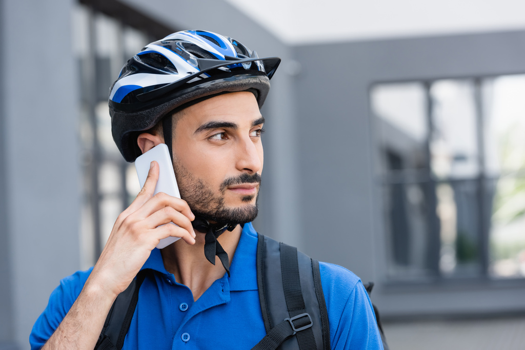 Мусульманский курьер в защитном шлеме разговаривает по мобильному телефону на улице  - Фото, изображение