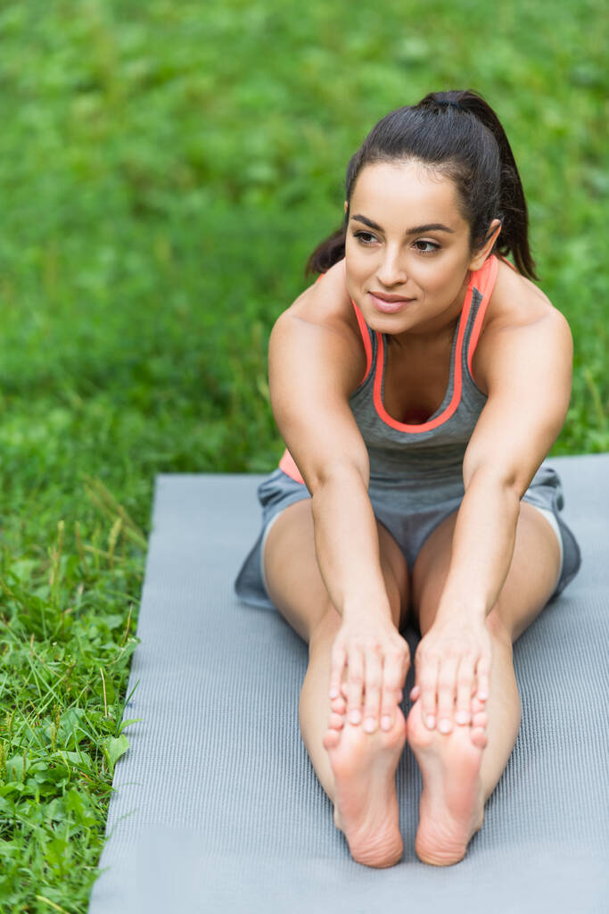 elastyczna i boso kobieta w odzieży sportowej rozciągająca się na macie do jogi w parku - Zdjęcie, obraz