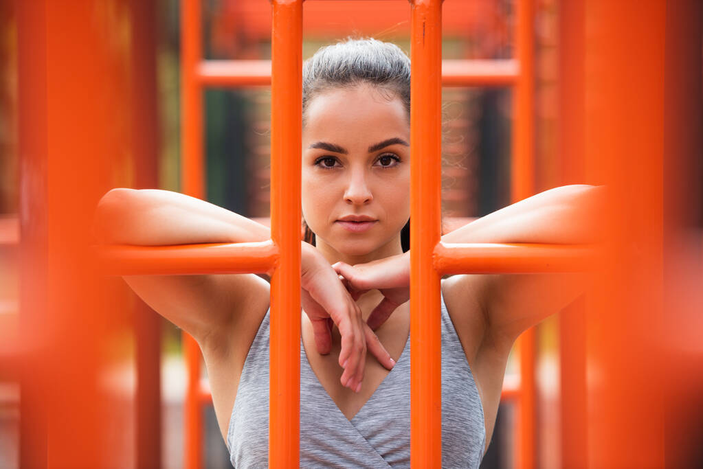 ταιριάζει γυναίκα σε αθλητικά ρούχα κοιτάζοντας κάμερα κοντά πορτοκαλί κάθετη σκάλα έξω - Φωτογραφία, εικόνα