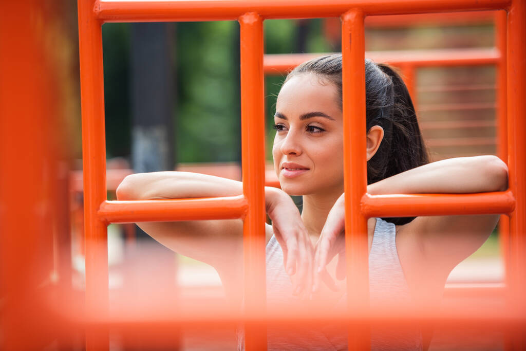 улыбающаяся спортсменка смотрит в сторону оранжевой вертикальной лестницы снаружи - Фото, изображение