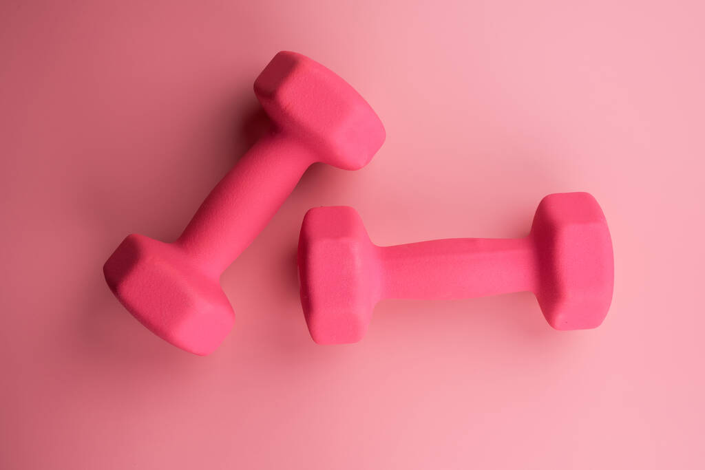 Due manubri femminili rosa isolati su sfondo rosa primo piano con spazio su copia. Concetto di fitness, perdita di peso e attività sportiva, vista dall'alto, flat lay - Foto, immagini
