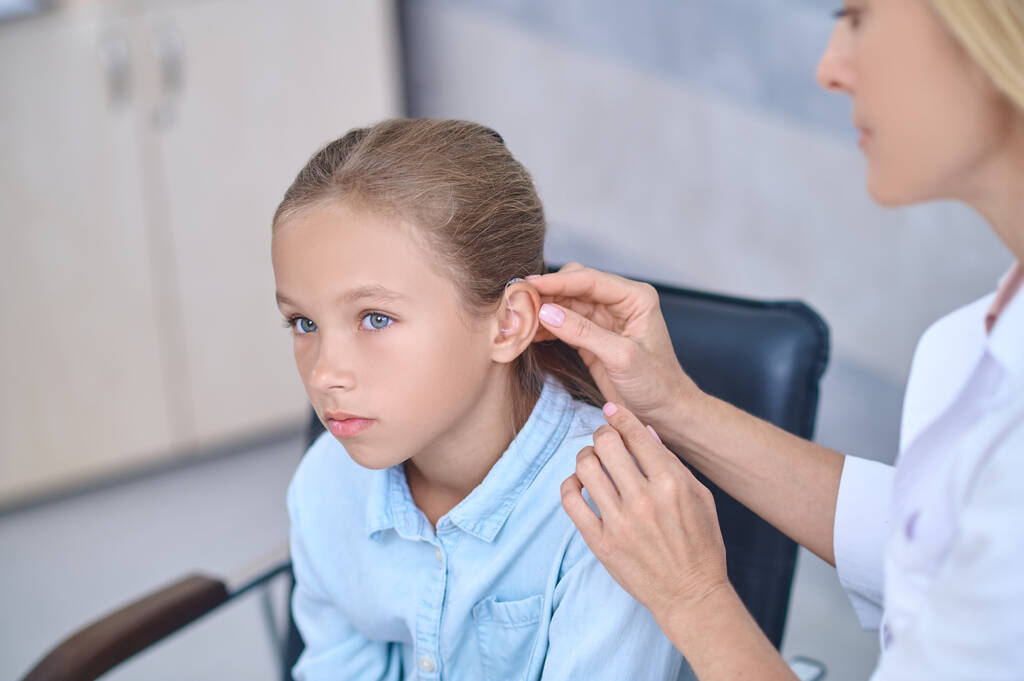 Médico calificado arreglando una ayuda para sordos detrás de la oreja de las chicas - Foto, imagen