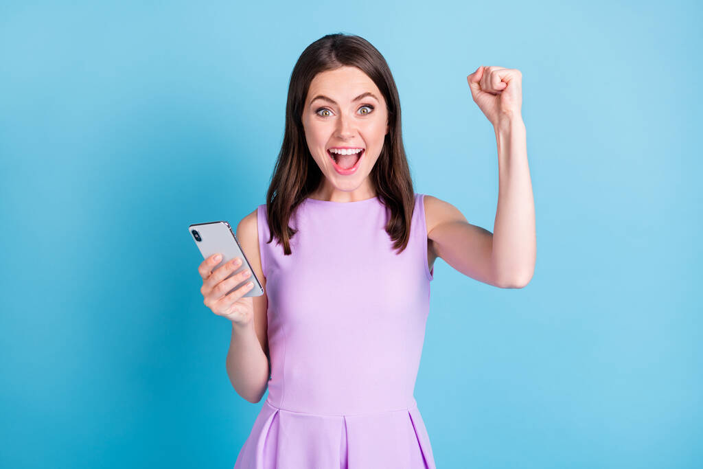 Photo of beautiful happy win young woman raise fist yeah hold smartphone message isolated on blue color background - Photo, Image