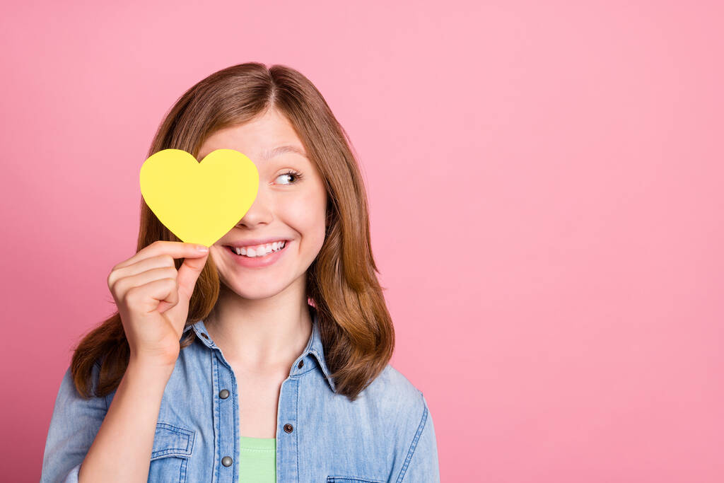 Foto Porträt Mädchen lächelnd versteckt Auge hinter gelben Herz Postkarte suchen Kopierraum isoliert pastellrosa Farbe Hintergrund - Foto, Bild