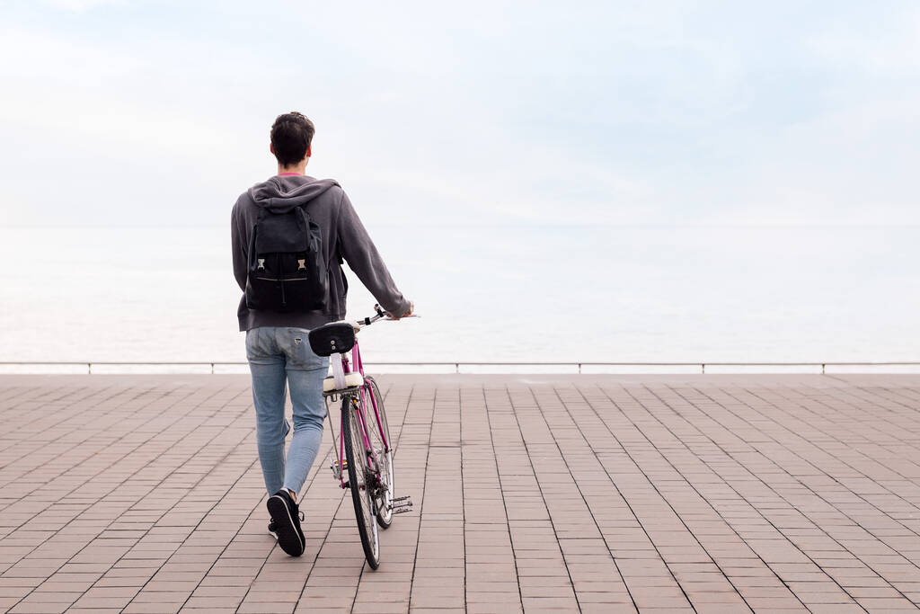 tylny widok nierozpoznawalnego młodzieńca pchającego rower, koncepcja ekologicznego i zrównoważonego transportu, przestrzeń na tekst - Zdjęcie, obraz