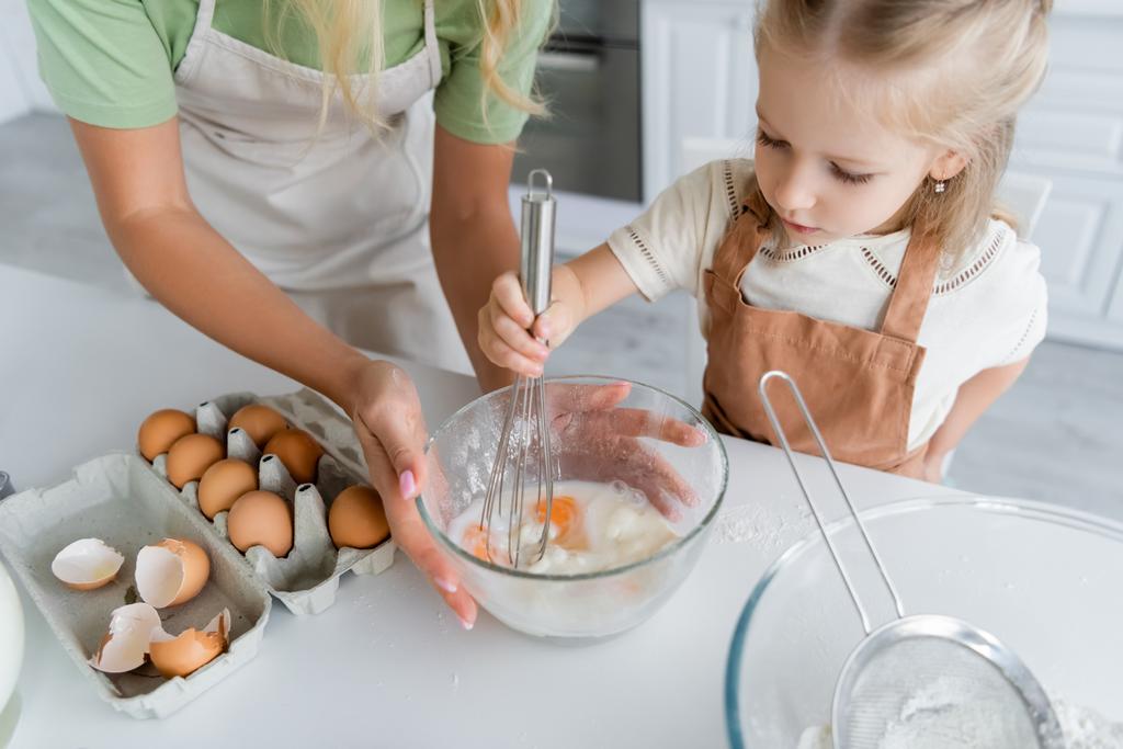 bambino mescolando uova di pollo e farina con frusta vicino alla madre che tiene ciotola - Foto, immagini