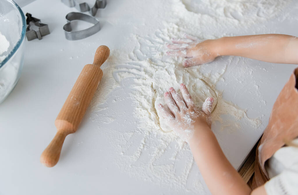 high angle view of cropped child kneading dough near rolling pin and cookie cutters - Photo, Image