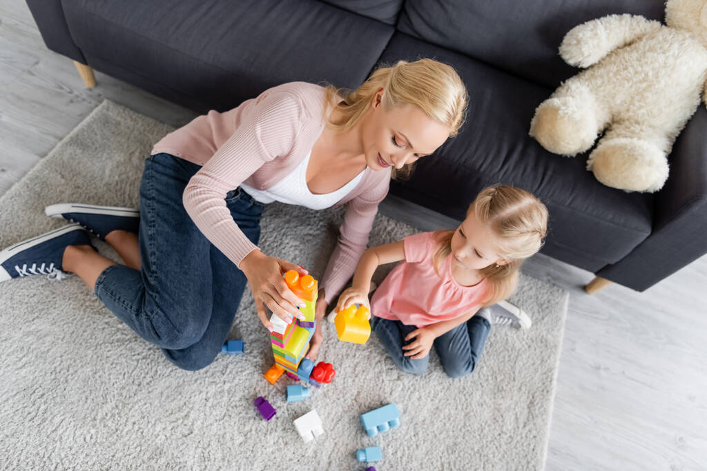 Вид сверху на мать и дочь, играющих со строительными блоками на полу дома - Фото, изображение