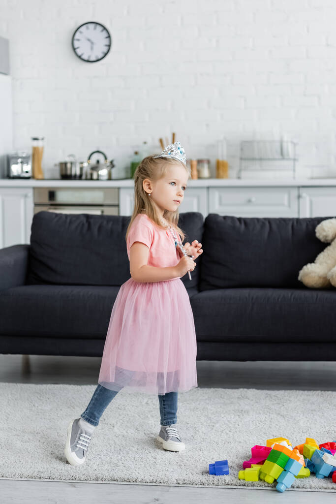 meisje in speelgoed kroon en tule rok staande met toverstaf thuis - Foto, afbeelding