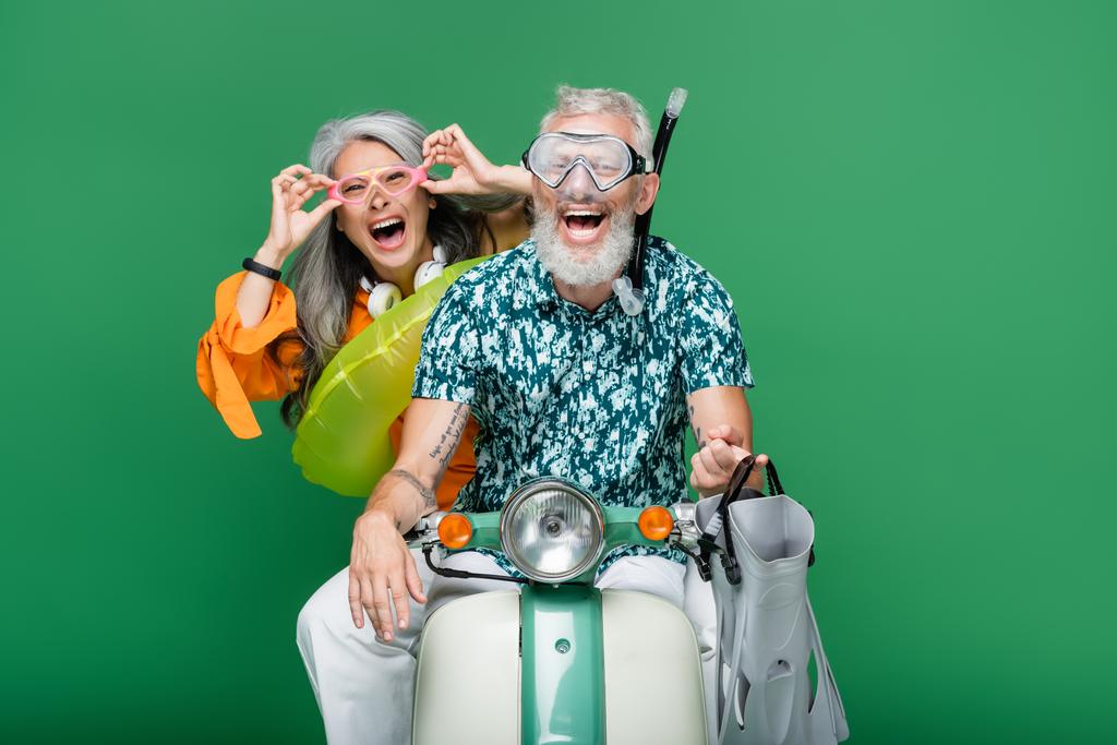 πολυεθνικό και ενθουσιασμένοι μεσήλικες ζευγάρι σε γυαλιά ιππασίας μοτοποδήλατο απομονωμένο σε πράσινο - Φωτογραφία, εικόνα