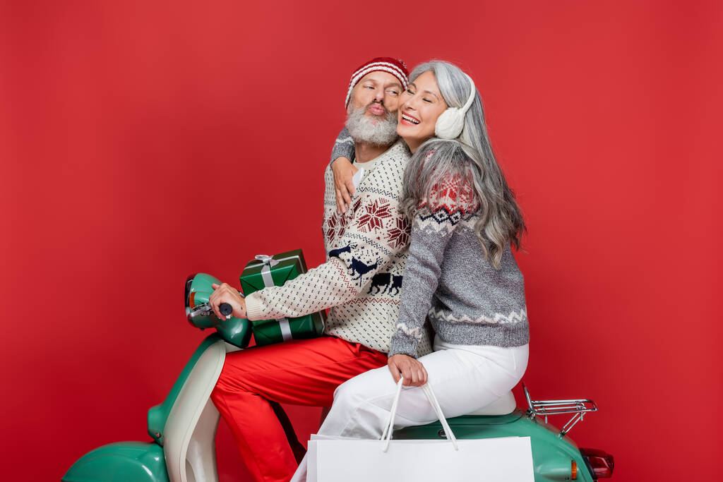 uomo di mezza età con Natale presenta labbra pouting vicino moglie asiatica mentre guida motorino su rosso - Foto, immagini