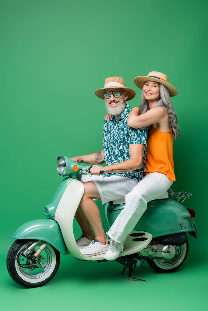 Güneş şapkalı mutlu Asyalı kadın ve yeşil motosikletli orta yaşlı koca.  - Fotoğraf, Görsel