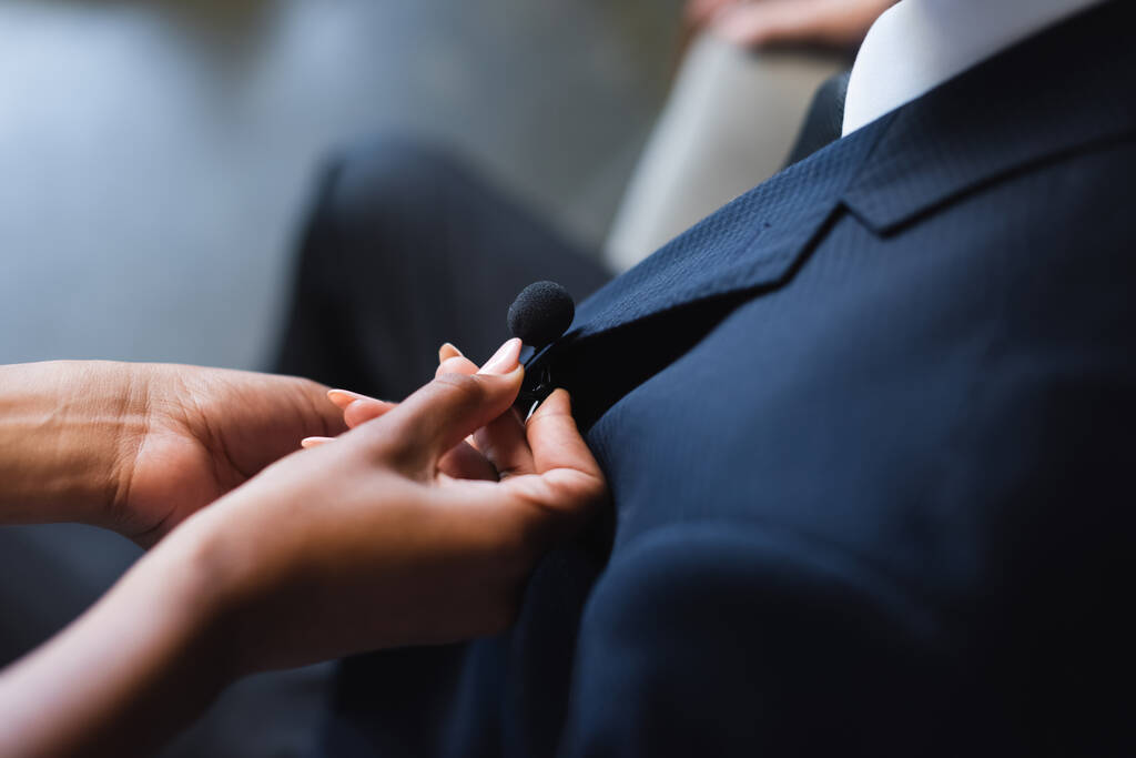 vista cortada de assistente americano africano ajustando microfone em terno de homem de negócios - Foto, Imagem