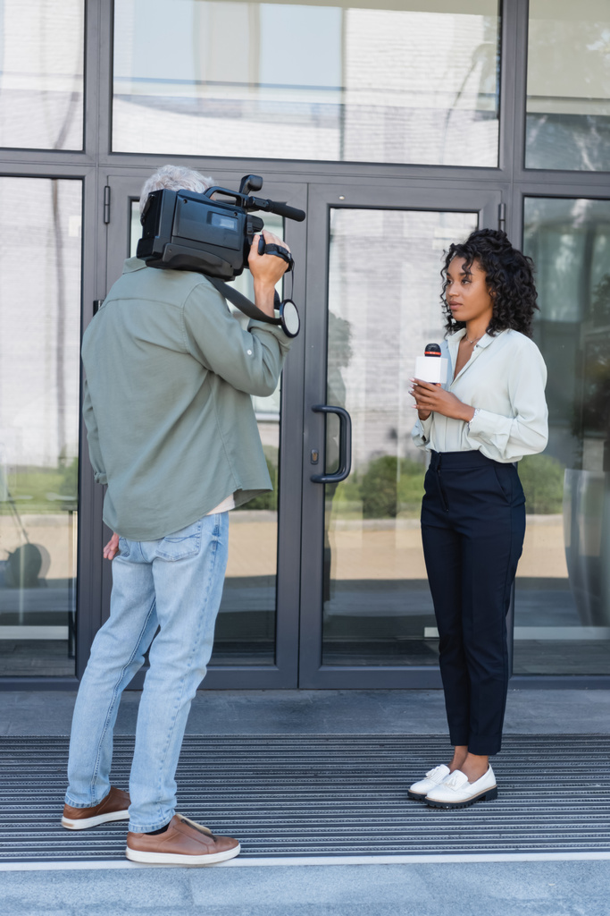 toute la longueur du journaliste afro-américain faisant reportage près de cameraman à l'extérieur - Photo, image