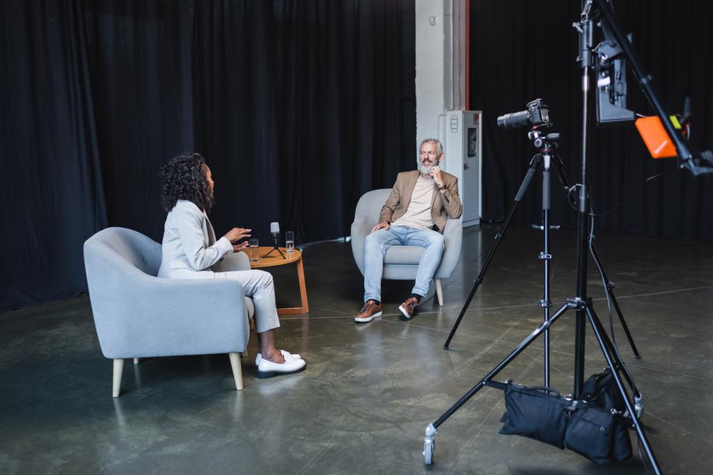 Американський журналіст-афроамериканець розмовляє з усміхненим бізнесменом, який сидить у кріслі під час інтерв'ю. - Фото, зображення