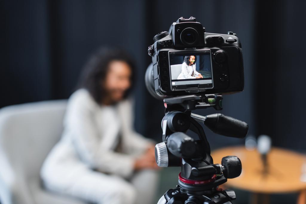 digitale camera op statief met afrikaanse Amerikaanse journalist zittend in fauteuil op scherm  - Foto, afbeelding