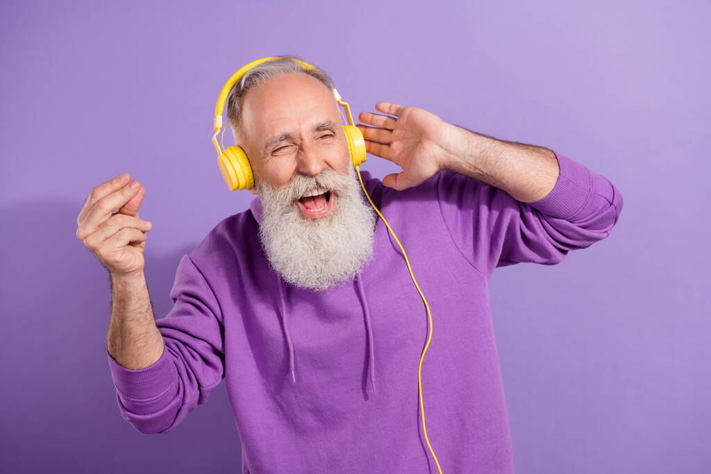 Retrato de un atractivo anciano alegre hombre de pelo gris escuchando golpear el baile estéreo divirtiéndose aislado sobre el fondo violeta violeta - Foto, imagen
