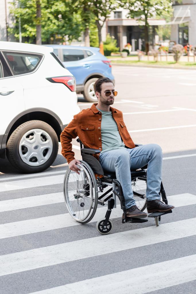 Behinderter Mann im Rollstuhl überquert Straße neben Autos in der Stadt - Foto, Bild