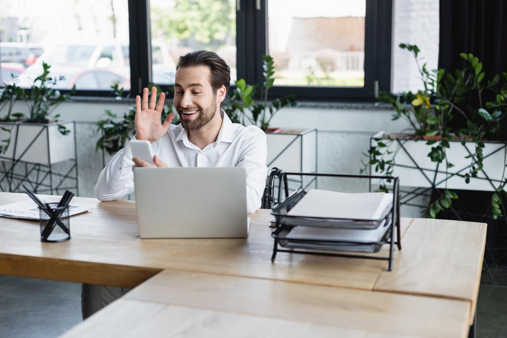 empresário desativado alegre acenando a mão durante chamada de vídeo no laptop no escritório - Foto, Imagem