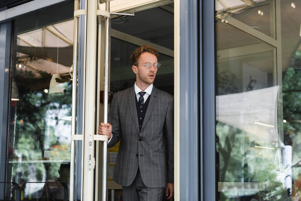 krullende zakenman in bril deur openen terwijl het verlaten van cafe  - Foto, afbeelding