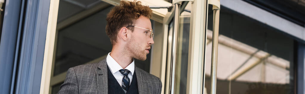 curly businessman in glasses looking away while leaving cafe, banner - Photo, Image