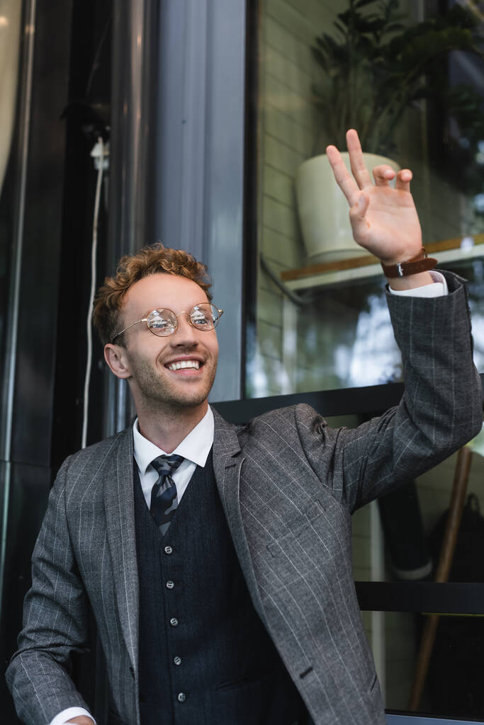 счастливый бизнесмен в очках с поднятой рукой вызывая официанта на террасе кафе  - Фото, изображение