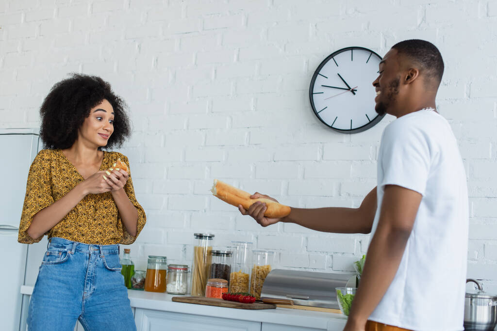 Африканский американец держит багет рядом с девушкой на кухне  - Фото, изображение