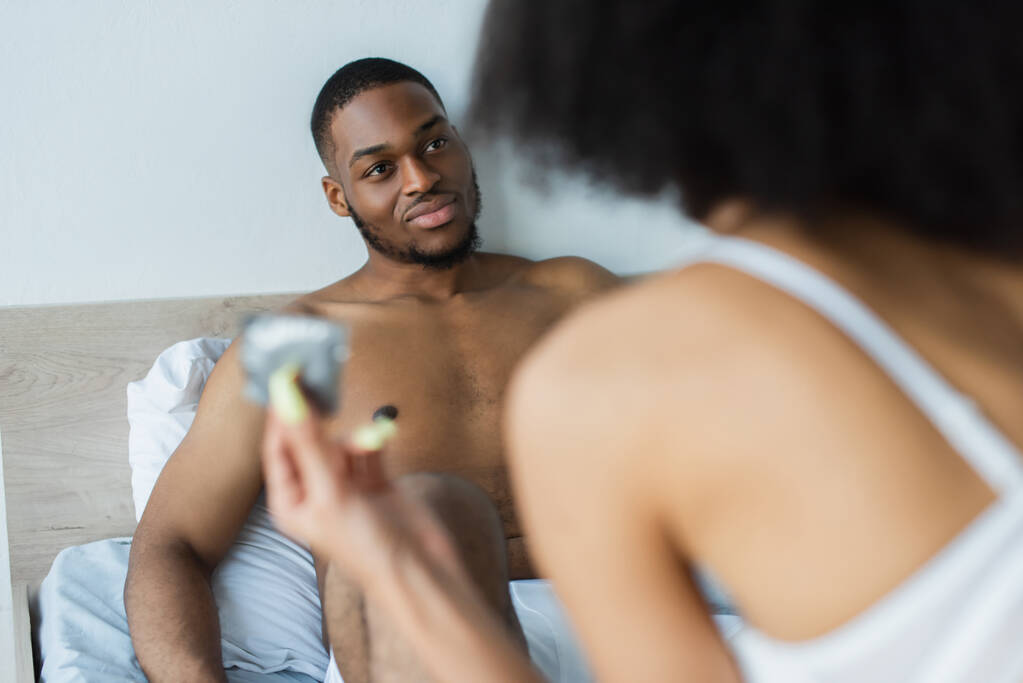 アフリカ系アメリカ人男見ますぼやけたガールフレンドとともにコンドームをつけませんでベッドルーム  - 写真・画像