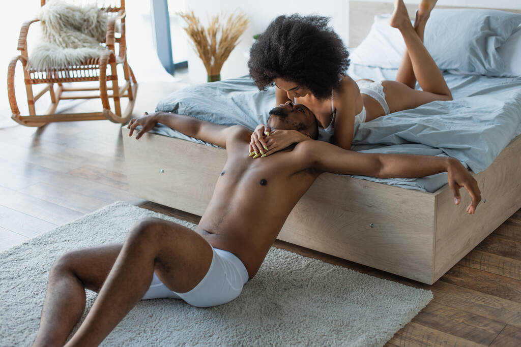 Молодая африканская американка в нижнем белье обнимает своего парня в спальне  - Фото, изображение