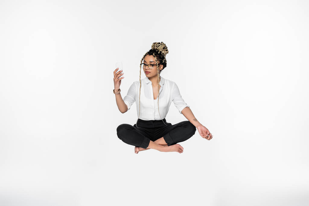 barefoot african american businesswoman with smartphone levitating in lotus pose isolated on white - Photo, Image