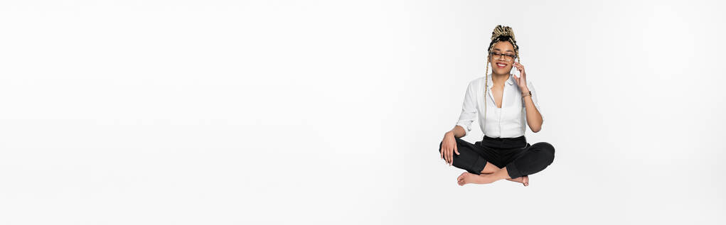 boldog afro-amerikai üzletasszony lebegő lótuszban pózol, miközben beszél okostelefon elszigetelt fehér, banner - Fotó, kép