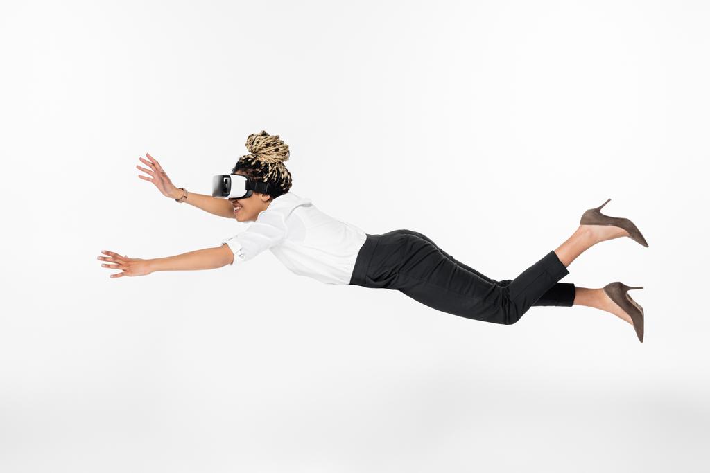 Seitenansicht der freudigen afrikanisch-amerikanischen Geschäftsfrau fliegen in vr Headset isoliert auf weiß  - Foto, Bild