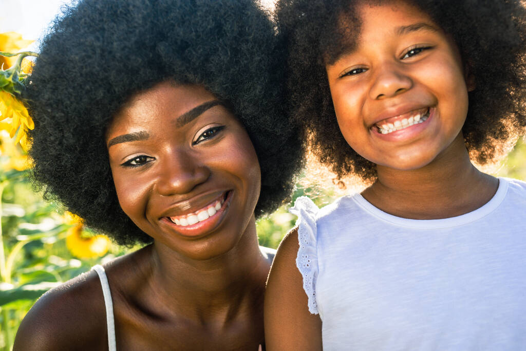 mooi afro-amerikaans mam en dochter smakelijk en het hebben van plezier in een zonnebloemen veld - Foto, afbeelding