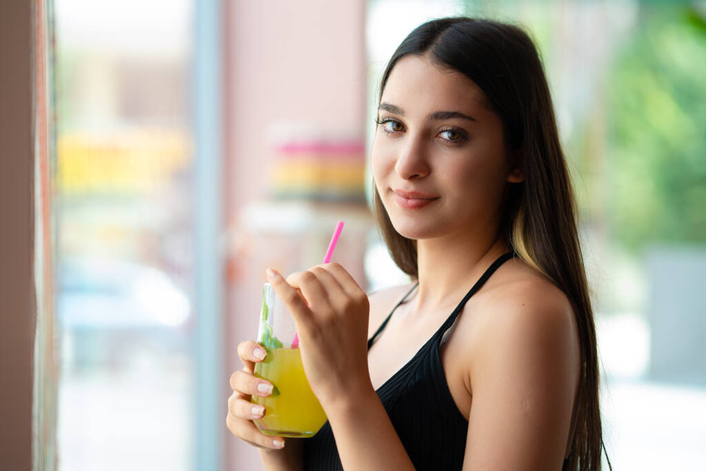 Jeune femme souriant et buvant une boisson devant la fenêtre. - Photo, image