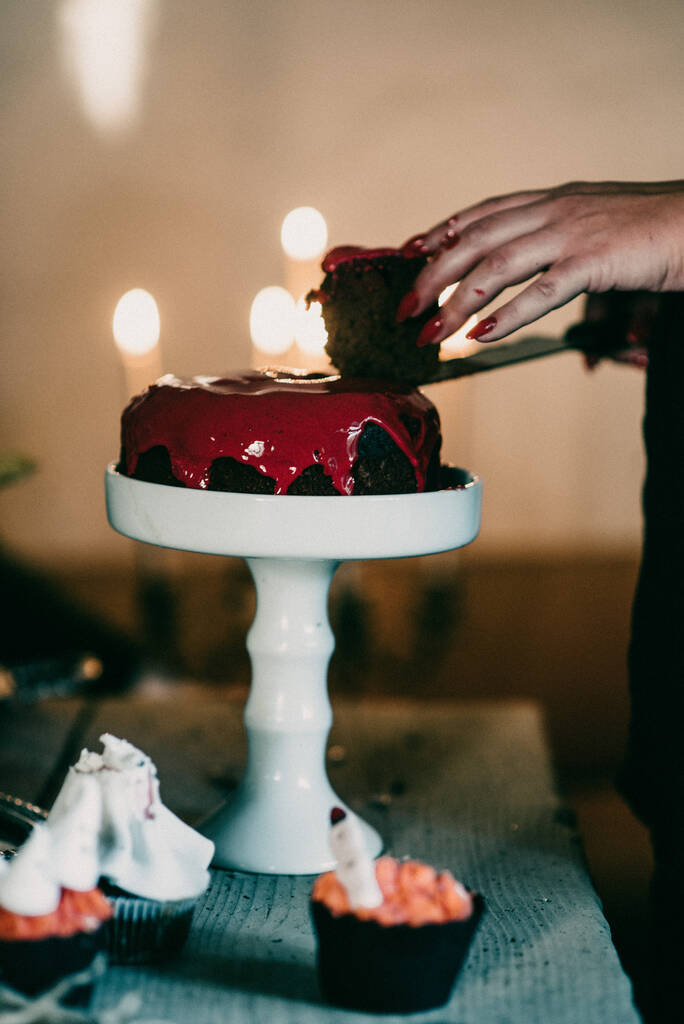 Eine vertikale Aufnahme einer Frau, die eine gruselige Halloween-Torte mit rotem Zuckerguss schneidet - Foto, Bild